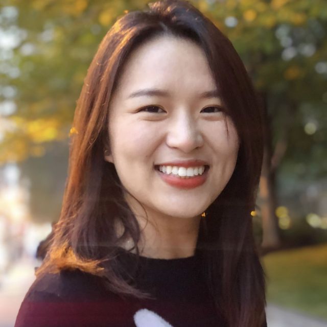 Xiaoxiao smiling in front of trees with yellow leaves